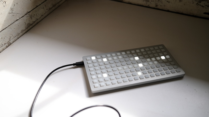 monome grid controller, a flat aluminium grid of backlit buttons, lit and connected by a USB cable